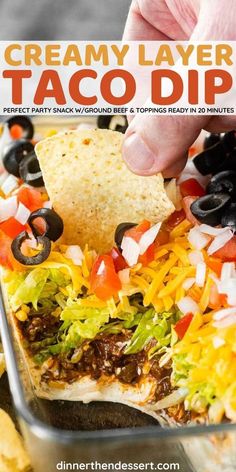 a hand dipping a tortilla chip into a casserole dish with black olives and cheese