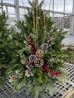 a christmas centerpiece with pine cones, berries and evergreens on a table in a greenhouse