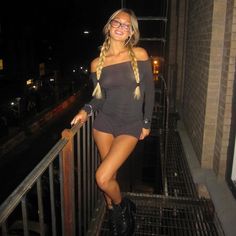 a woman in short shorts and boots standing on a balcony at night with her hand on the railing