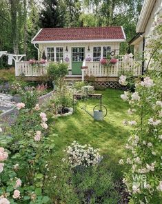 a small white house surrounded by flowers and greenery