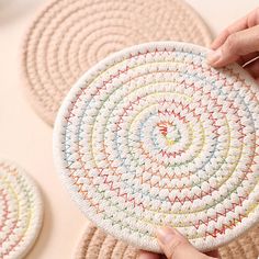 someone is holding up a crocheted coaster in front of three other round rugs