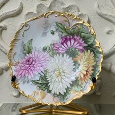 a plate with flowers painted on it is sitting on a stand next to a wall