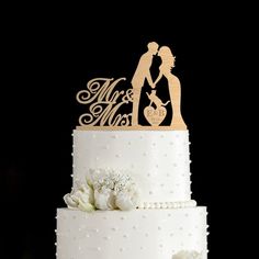 a white wedding cake with a wooden topper and bride and groom holding hands on it