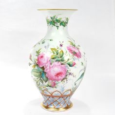 a vase with flowers painted on it sitting on a white tableclothed surface and gold trimming around the edges