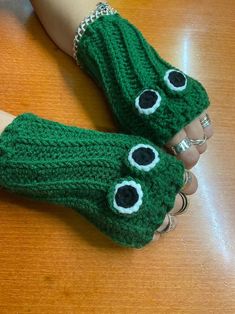 two hands wearing green knitted mittens with eyes