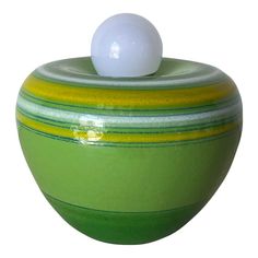 a green and yellow striped ceramic container with a white ball on it's top