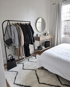 a bedroom with a bed, mirror and coat rack in the corner next to a window