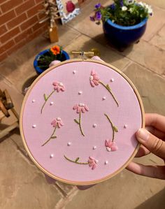 a person holding up a pink embroidered object with small flowers on the front and side