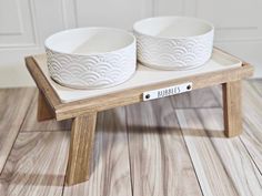 two white bowls sitting on top of a wooden stand