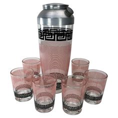 a set of pink glasses and a jug with greek designs on the side, all lined up in front of each other