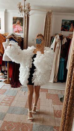 a woman taking a selfie in front of a mirror wearing a white feathered dress