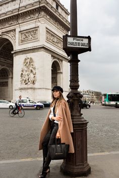 a woman leaning on a lamp post in front of the arc de trioe triumph