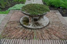 a dog is sitting in the middle of a brick garden fountain with moss growing on it's sides