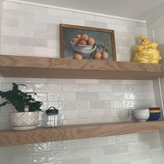 two wooden shelves with pots and bowls on them in a white tiled kitchen, next to a yellow duck statue