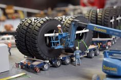 a toy truck with two men working on it's tires in the middle of an assembly line