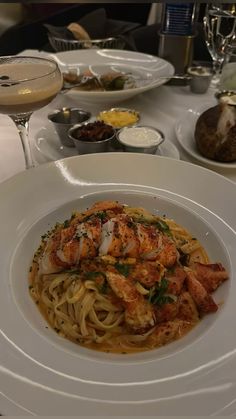 a white plate topped with pasta and shrimp next to glasses of wine on a table