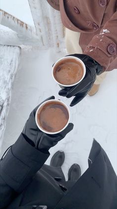 two cups of hot chocolate are being held by someone in black gloves and mittens