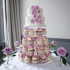 a wedding cake and cupcakes on a table with flowers in the vases