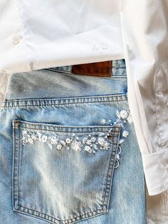 the back pocket of a pair of jeans with embroidered flowers on them and a white shirt in the background