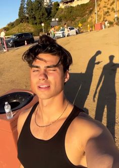 a young man standing next to a trash can on the side of a road with his shadow