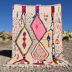 a multicolored area rug on gravel with cactus in the background