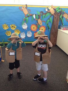 two young boys wearing safari hats and vests, standing in front of a bulletin board