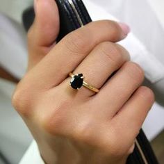 a woman's hand holding a ring with a black diamond on it, while wearing a white shirt