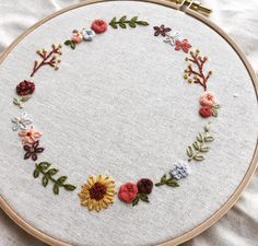 a close up of a embroidery on a hoop with flowers and leaves around the hoop