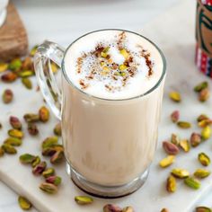 a glass mug filled with white liquid surrounded by pistachios