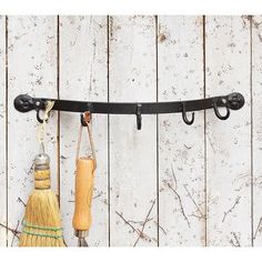 two brooms hanging from hooks on a white wooden wall