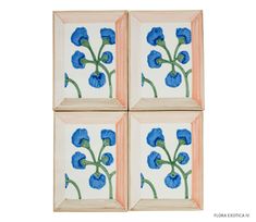 four blue flowers are painted on three square tile pieces, each with an orange border