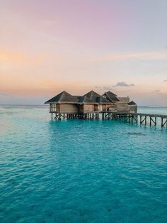 two huts on stilts in the ocean at sunset