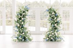 two tall floral arrangements in front of large windows with white and blue flowers on them