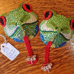 two green and red beaded frog hats on a wooden table next to a tag