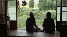 two people sitting in front of an open door looking out at a field and trees