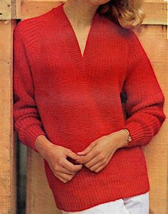 a woman wearing a red sweater and white pants standing in front of a wooden wall