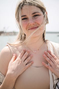 a woman standing on the beach with her hands in her chest and looking at the camera