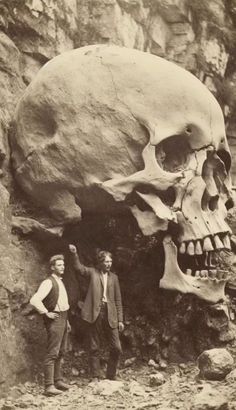 two men standing next to a giant skull