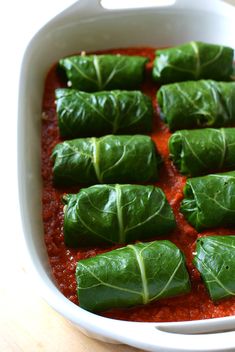 some green leafy vegetables are in a white casserole dish on a wooden table