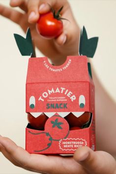 a person holding up a tomato and some food in a box that is shaped like a carton