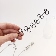 a hand holding some wire in front of a vase