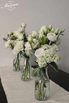 three vases filled with white flowers on top of a tablecloth covered table cloth