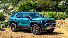 a blue truck parked on top of a dirt road next to rocks and trees in the background