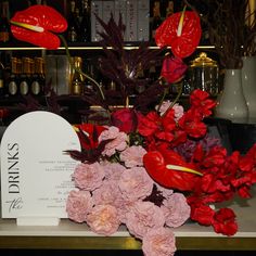 red flowers and pink carnations sit on a table in front of a sign