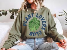 "Plant Lovers Club" Sweatshirt - Join the Green Revolution Calling all plant enthusiasts! Show off your green thumb and membership in the "Plant Lovers Club" with this cozy sweatshirt. Perfect for anyone who's passionate about houseplants, gardening, or simply being surrounded by greenery. Whether you're potting new plants or lounging in your indoor jungle, this sweatshirt is a must-have for every plant lover. A perfect gift for plant parents or a great treat for yourself to proudly wear your pl Casual Crew Neck Sweatshirt With Plant Print, Crew Neck T-shirt With Plants Print, Botanical Plants Print Crew Neck T-shirt, Plant Lover Shirt, Plant Sweatshirt, Green Revolution, Club Sweatshirts, Indoor Jungle, Plant Lady