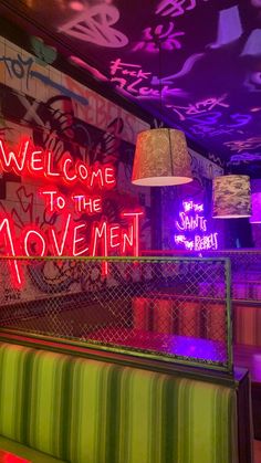 a neon sign that says welcome to the movement in front of a colorful wall with graffiti on it