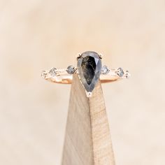 a ring with a pear shaped black diamond and three white diamonds on the band, sitting on top of a wooden stand