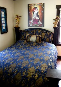 a bed with blue and gold comforter in a bedroom next to a window, framed artwork on the wall