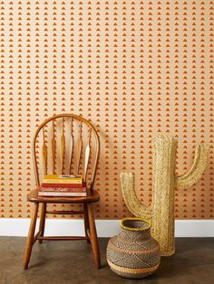 a wooden chair next to a wall with an orange pattern on it and a cactus