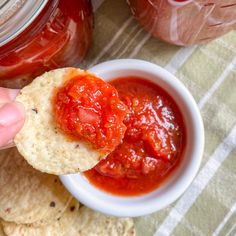 a hand holding a piece of bread that has been dipped with ketchup and surrounded by tortilla chips